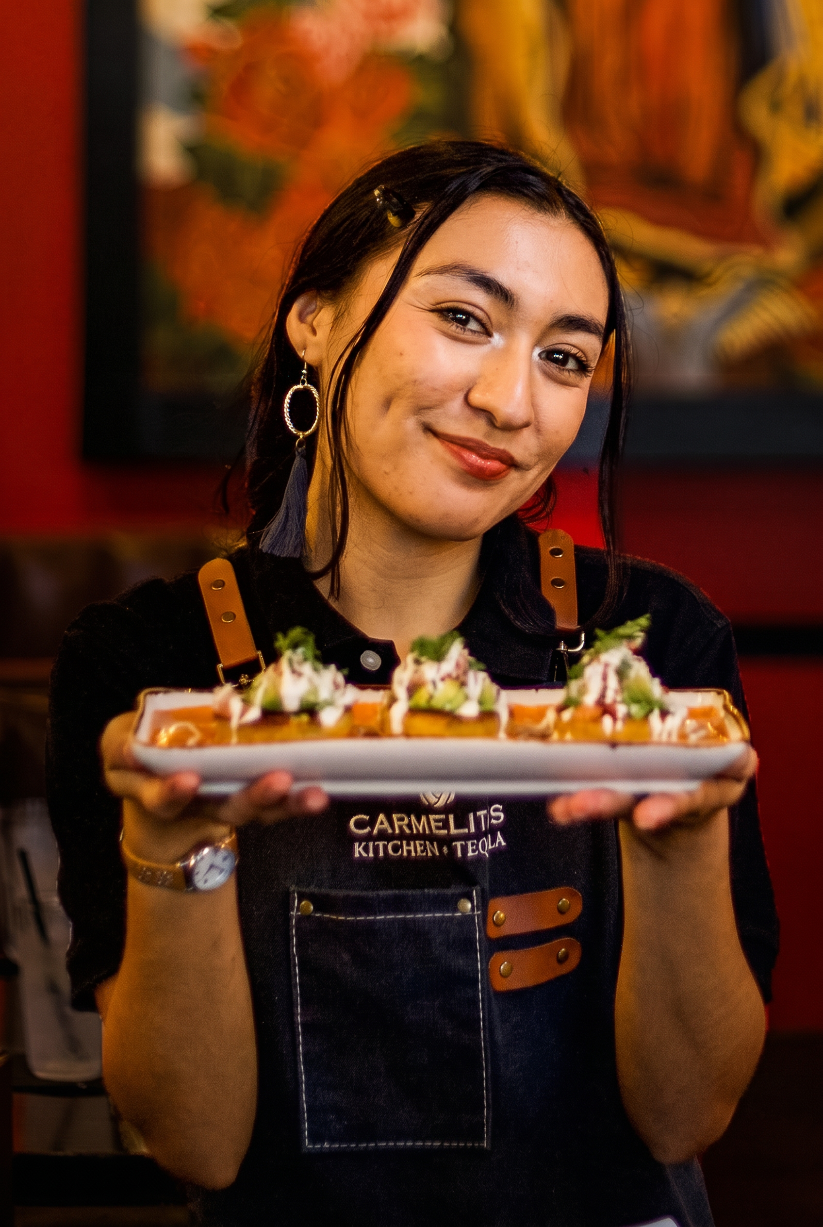 Houston restaurant photography of a smiling server holding a plate of flautas topped with cream and guacamole